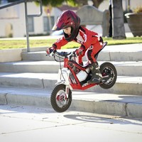 4 year old girl riding a small electric motorbike down four concrete steps and wearing a full-face crash helmet, riding gear, gloves and boots.  